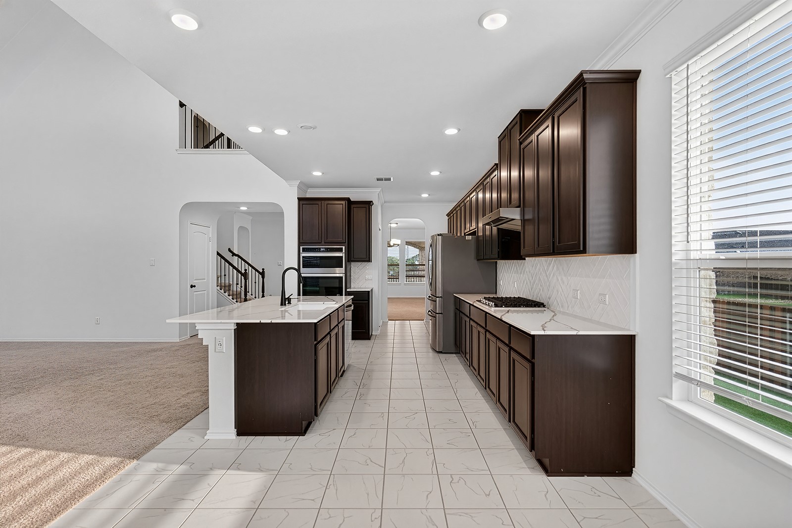 4600 Ercolano Lane Round Rock, TX 78665 - Photo 12 of 37 Modern kitchen featuring dark wood cabinetry, light tile flooring, built-in stainless steel appliances, a center island with sink, and light-toned countertops