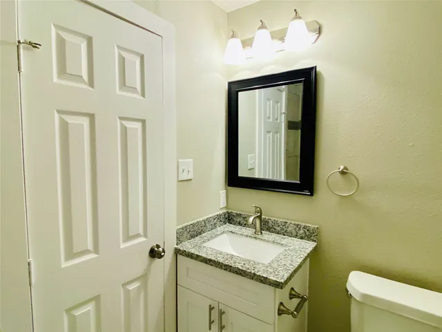a bathroom with a granite countertop sink vanity mirror and toilet