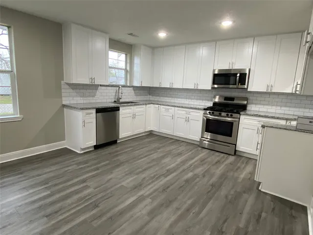 a kitchen with granite countertop wooden floors stainless steel appliances and sink