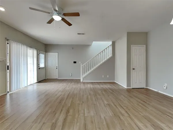 an empty room with wooden floor ceiling fan and windows
