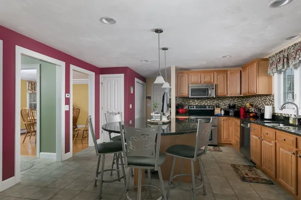 a kitchen with stainless steel appliances granite countertop a stove top oven a refrigerator a sink and chairs