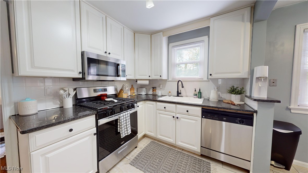 4042 Bushnell Road University Heights, OH 44118 - Photo 9 of 37 Kitchen featuring sink, backsplash, white cabinetry, stainless steel appliances, and dark stone counters
