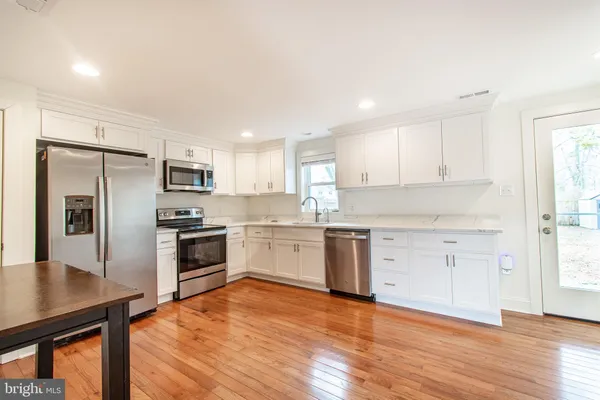 a kitchen with granite countertop a refrigerator oven a sink dishwasher and white cabinets with wooden floor