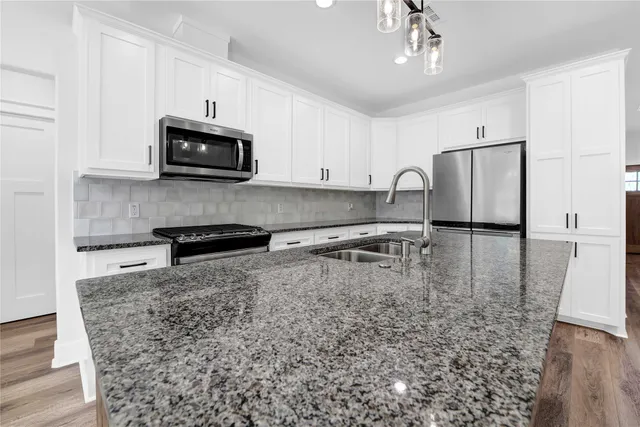 a kitchen with stainless steel appliances granite countertop a stove a refrigerator a sink a microwave oven with white cabinets and granite countertops