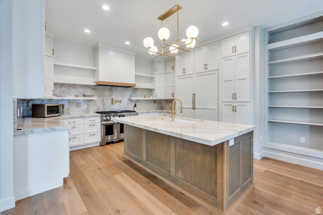 250 South Main Street, Unit 10 Alpine, UT 84004 - Photo 4 of 29 Gourmet kitchen featuring a large central island with a stone countertop, light wood-finish flooring, full-height stone slab backsplash, stainless steel range with custom hood, and extensive built-in cabinetry