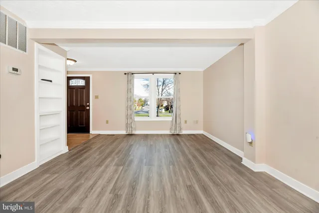 a view of an empty room with wooden floor and a window