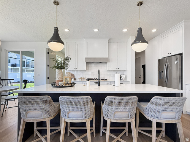 916 Rocky Mountain Way Elk Ridge, UT 84651 - Photo 15 of 54 Kitchen featuring a spacious island, light wood-type flooring, a textured ceiling, light stone countertops, and a kitchen breakfast bar