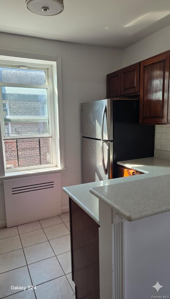 33-16 82nd Street, Unit 6D Queens, NY 11372 - Photo 8 of 16 Kitchen with light tile patterned floors, freestanding refrigerator, a peninsula, light stone countertops, and a kitchen breakfast bar
