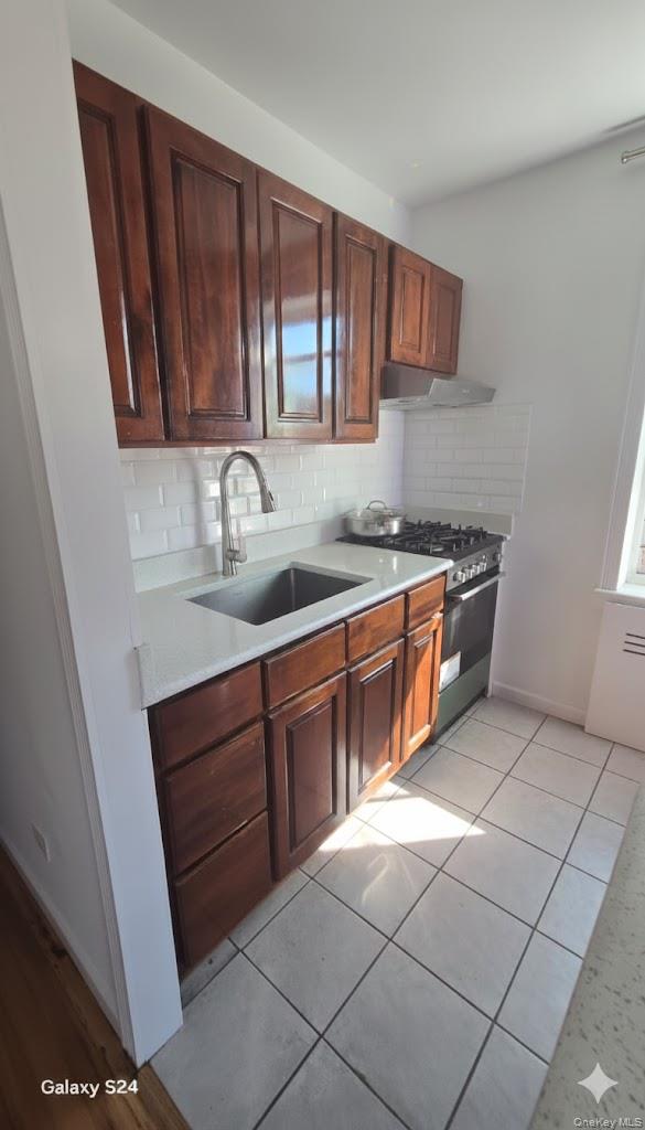 33-16 82nd Street, Unit 6D Queens, NY 11372 - Photo 9 of 16 Kitchen with stainless steel range with gas cooktop, decorative backsplash, under cabinet range hood, and light stone countertops