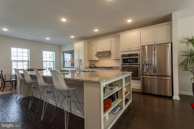 a kitchen with stainless steel appliances granite countertop a refrigerator a stove a sink a dining table and chairs