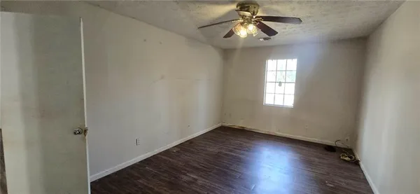 an empty room with wooden floor fan and windows