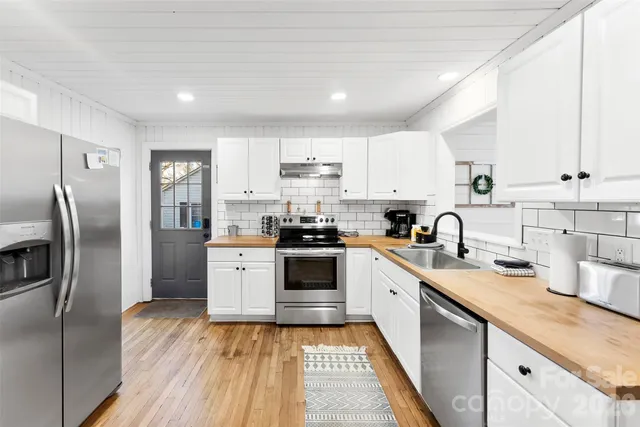 a kitchen with stainless steel appliances granite countertop a refrigerator a sink dishwasher a stove and white countertops with wooden floor