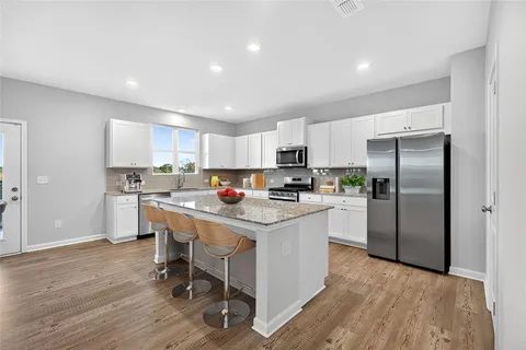 a kitchen with stainless steel appliances a refrigerator a sink dishwasher a stove top oven a refrigerator with white cabinets and wooden floor
