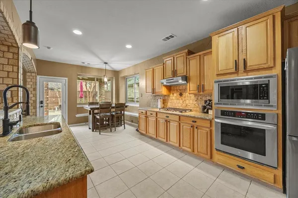 a kitchen with stainless steel appliances granite countertop a stove top oven a sink a dining table and chairs with wooden floor