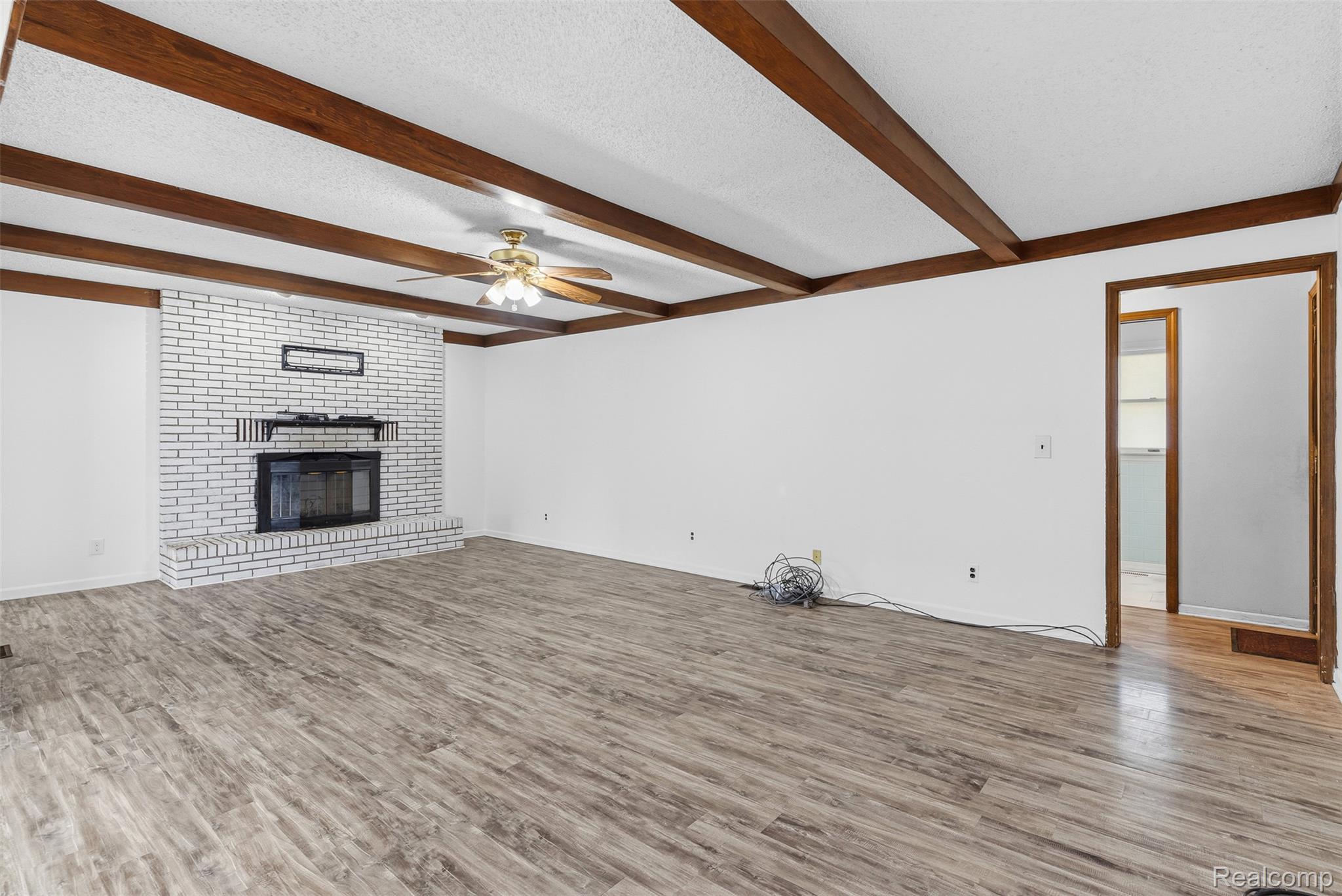 3432 South State Road Davison, MI 48423 - Photo 29 of 58 Unfurnished living room featuring wood finished floors, a brick fireplace, a textured ceiling, ceiling fan, and beam ceiling