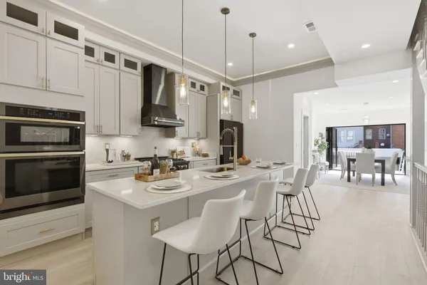 a kitchen with stainless steel appliances kitchen island granite countertop a stove a sink a oven a dining table and chairs with white cabinets