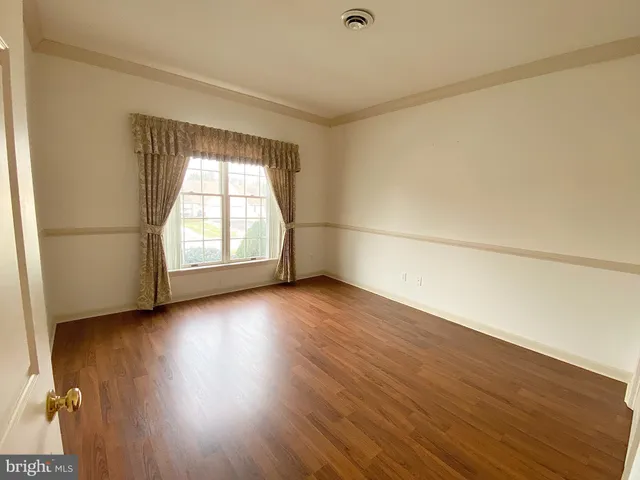 an empty room with wooden floor and windows with curtains