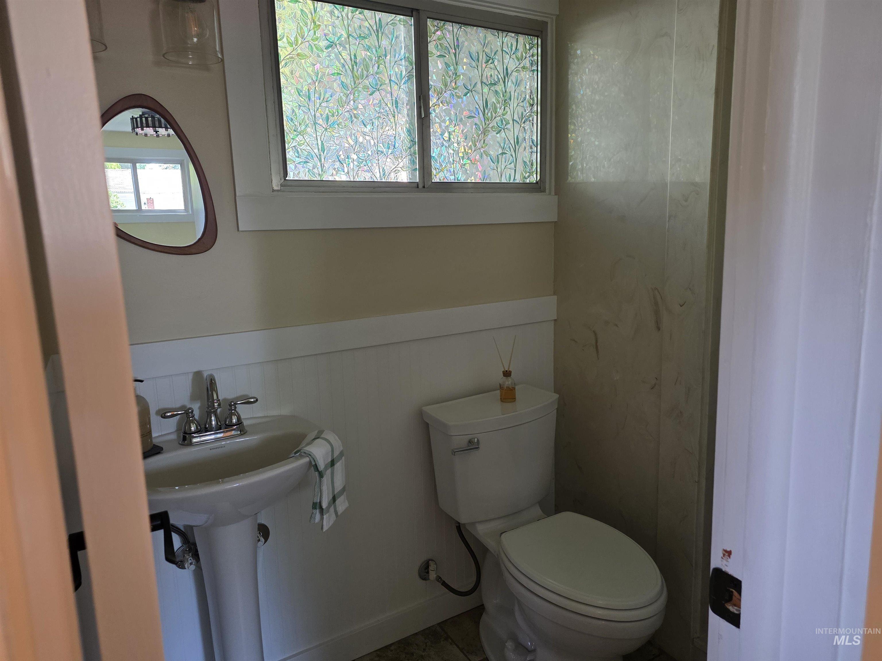 421 East Main Street Jerome, ID 83338 - Photo 12 of 13 Bathroom featuring wood-finish flooring, a white porcelain pedestal sink, a white bathtub with tile surround, a built-in storage unit with drawers and open shelving, and a window with trim