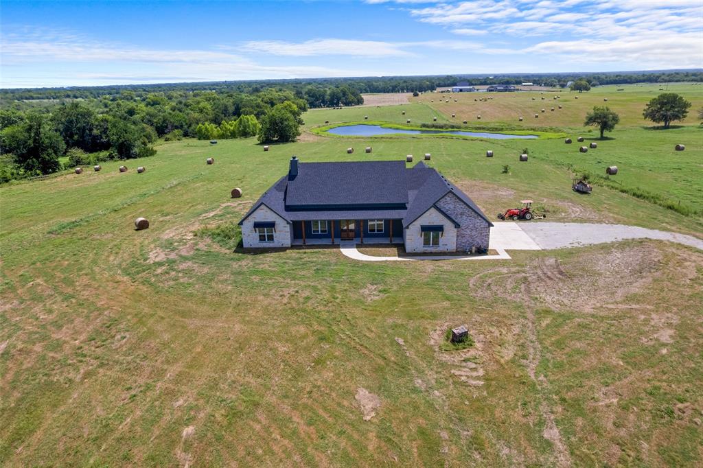 4411 Fm 751 Wills Point Wills Point, TX 75169 - Photo 39 of 40 Expansive rural property featuring a stone and siding residence with a dark roof, surrounded by open fields, trees, and water features