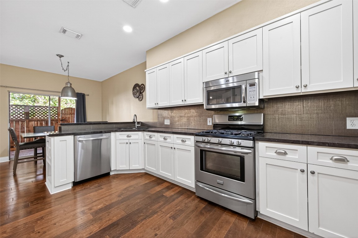 65 Scarlet Woods Court Spring, TX 77380 - Photo 11 of 36 This kitchen features modern stainless steel appliances, white cabinetry, and dark countertops. It's open to a dining area with hardwood floors and plenty of natural light from a large window.