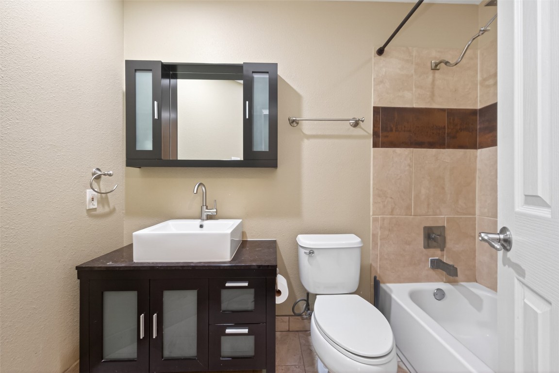 65 Scarlet Woods Court Spring, TX 77380 - Photo 14 of 36 This modern bathroom features a sleek vanity with a vessel sink and a dark wood cabinet. It includes a bathtub with a tiled shower area and neutral walls, providing a clean and contemporary look.