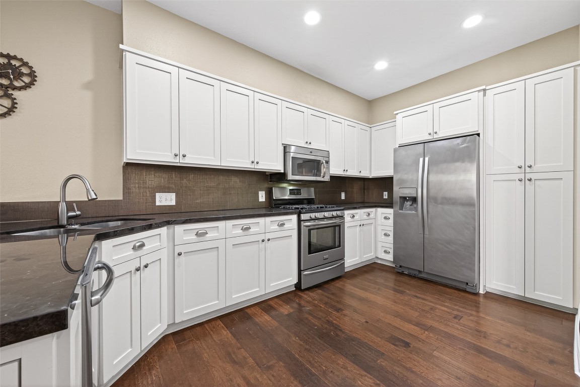 65 Scarlet Woods Court Spring, TX 77380 - Photo 9 of 36 This modern kitchen features sleek white cabinetry, stainless steel appliances, and dark countertops. It has ample storage space and a spacious layout with hardwood floors, ideal for cooking and entertaining.