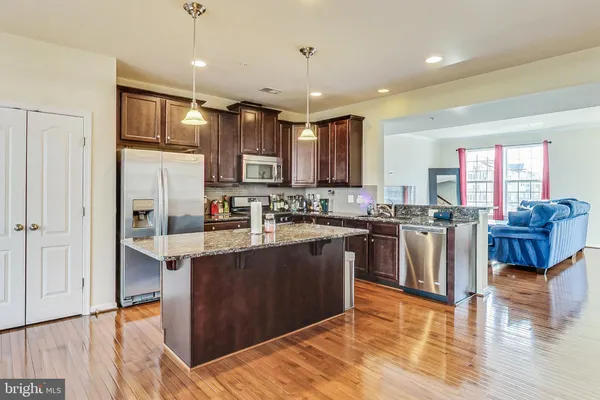 a kitchen with stainless steel appliances granite countertop a refrigerator a sink dishwasher a oven and a dining table with wooden floor