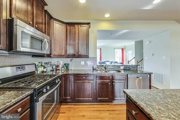 a kitchen with stainless steel appliances granite countertop a stove top oven a sink dishwasher and cabinets with wooden floor