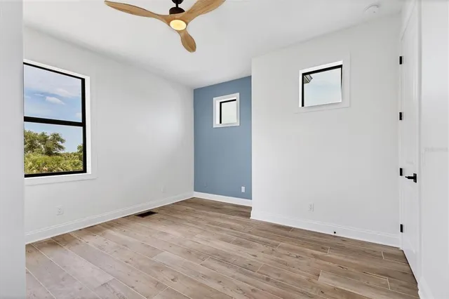 a view of an empty room with wooden floor and a ceiling fan