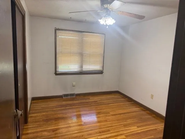 an empty room with wooden floor chandelier fan and windows