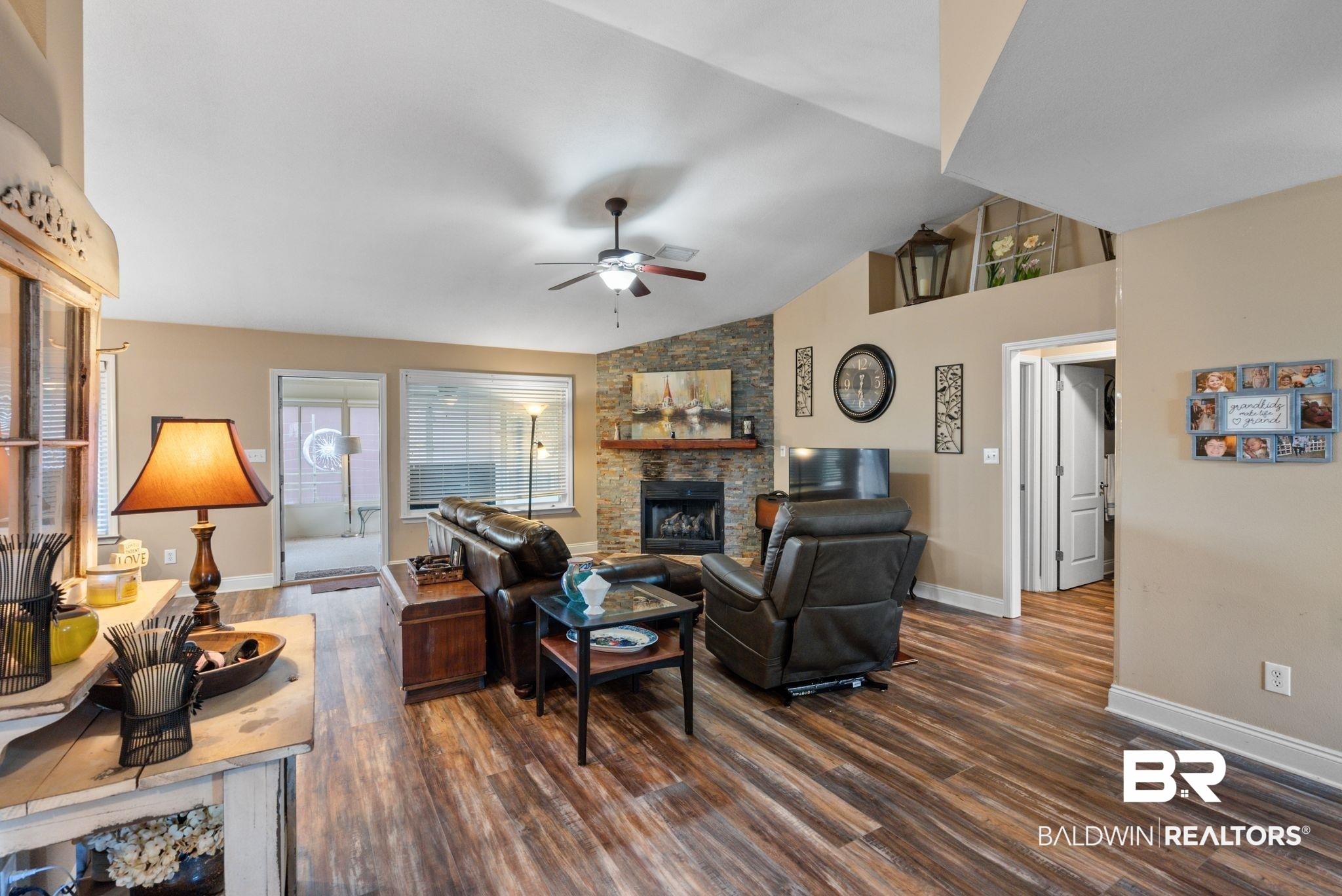 562 Vestige Mews Foley, AL 36535 - Photo 7 of 54 Living area featuring vaulted ceilings, wood-finish flooring, a stone-accented fireplace with a wood mantle, and a ceiling fan