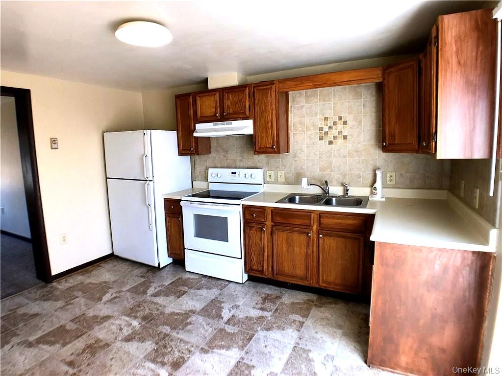 69 Old Unionville Road, Unit 4 Wallkill, NY 12589 - Photo 6 of 21 Kitchen featuring white appliances, light countertops, wood finish cabinetry, stone finish floors, and tasteful backsplash