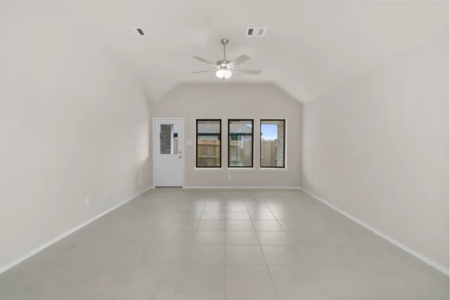 an empty room with chandelier fan and windows