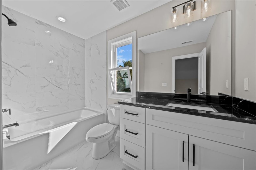 105 Bree Drive Anderson, SC 29621 - Photo 26 of 48 A well-appointed bathroom with gleaming marble-look tile, a crisp white vanity, and dark stone countertop.
