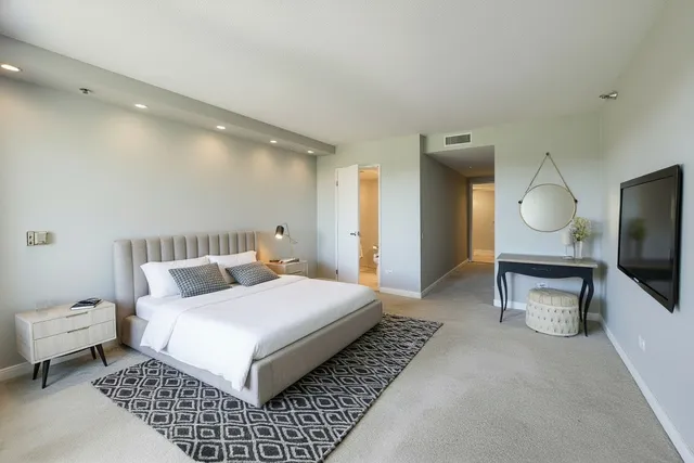 a spacious bedroom with a bed a mirror on dresser and a flat screen tv