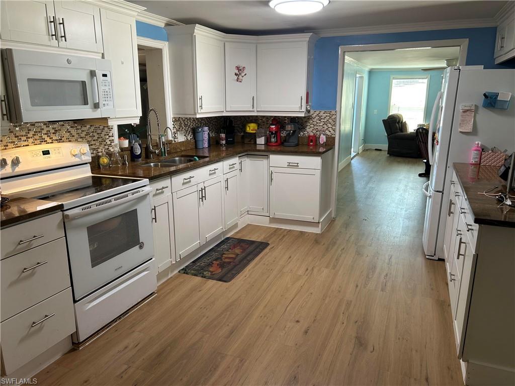 181 Pine Key Lane, Unit 29 Naples, FL 34114 - Photo 9 of 20 Kitchen featuring white appliances, white cabinets, light wood-style flooring, ornamental molding, and dark stone countertops