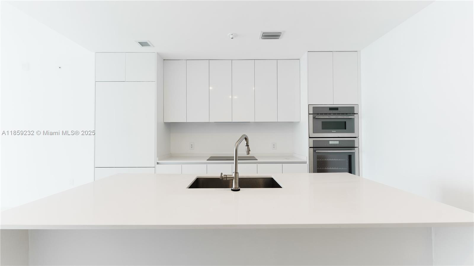 700 Northeast 24th Street, Unit 2705 Miami, FL 33137 - Photo 18 of 43 a kitchen with kitchen island a sink a stove and white cabinets