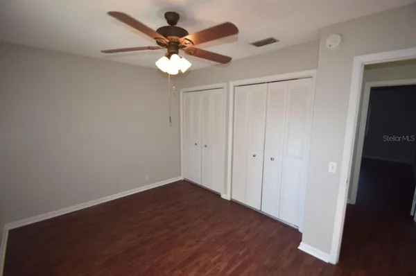 an empty room with wooden floor ceiling fan and window