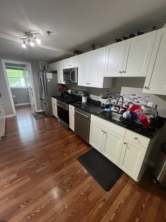 a kitchen with granite countertop a stove top oven a sink dishwasher and white cabinets with wooden floor