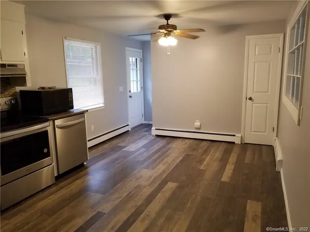 a view of an empty room with wooden floor and a ceiling fan