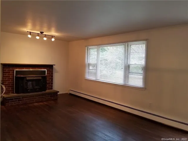 an empty room with wooden floor fireplace and windows