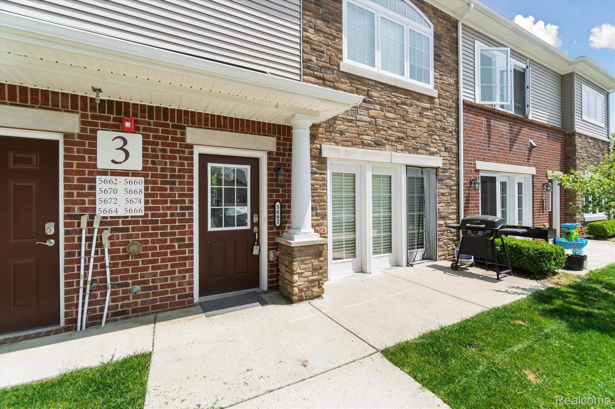 5662 Arbor Chase Drive Ann Arbor, MI 48103 - Photo 2 of 27 Multi-level townhome exterior featuring a combination of brick and stone facade, private entry door with transom window, ground-level patio space, and manicured lawn