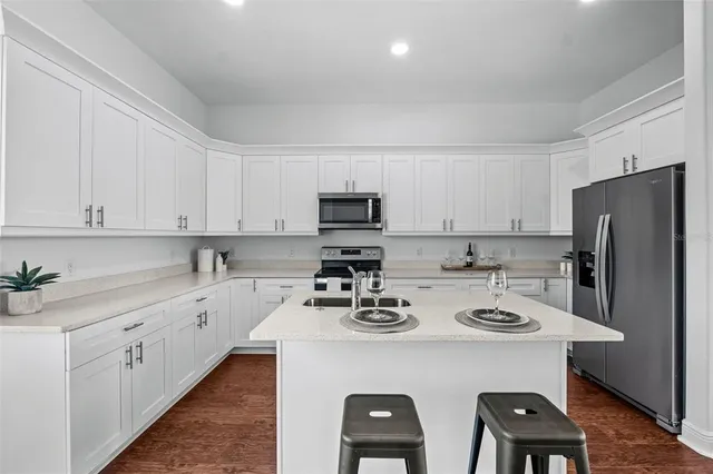 a kitchen with stainless steel appliances a sink a stove a refrigerator cabinets and chairs