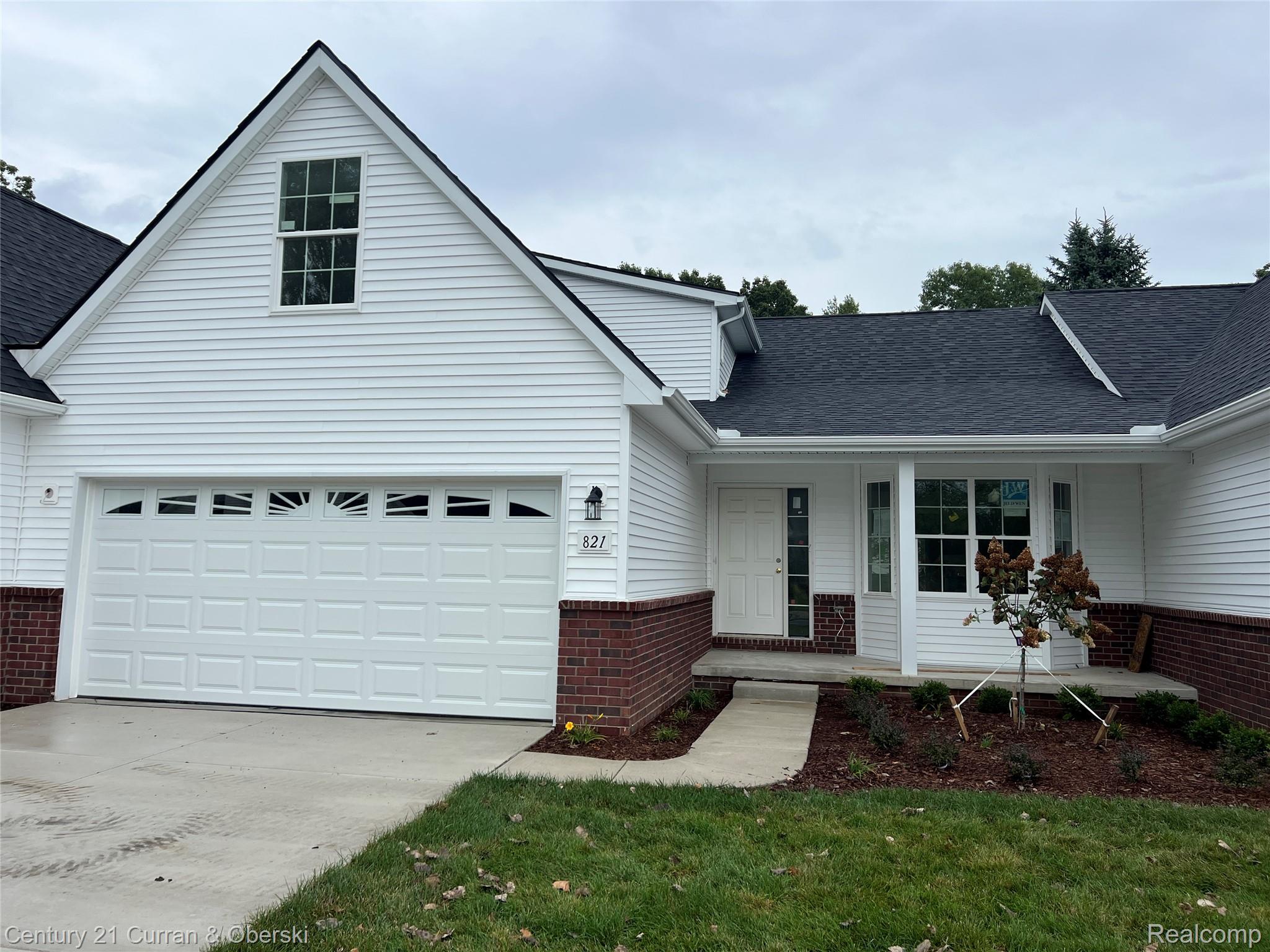 821 Nelson's Ridge Drive, Unit 12 Howell, MI 48843 - Photo 1 of 2 White vinyl siding exterior with dark shingle roof, red brick accent, attached two-car garage, and covered entryway