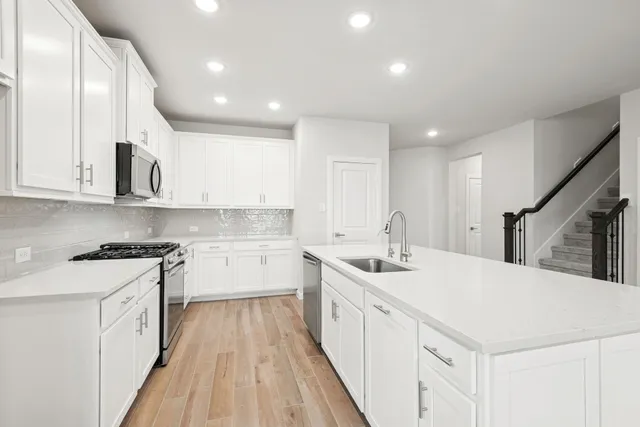 a large kitchen with stainless steel appliances granite countertop a large center island a stove a refrigerator with cabinets and wooden floor