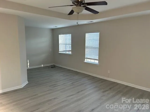 an empty room with wooden floor fan and windows