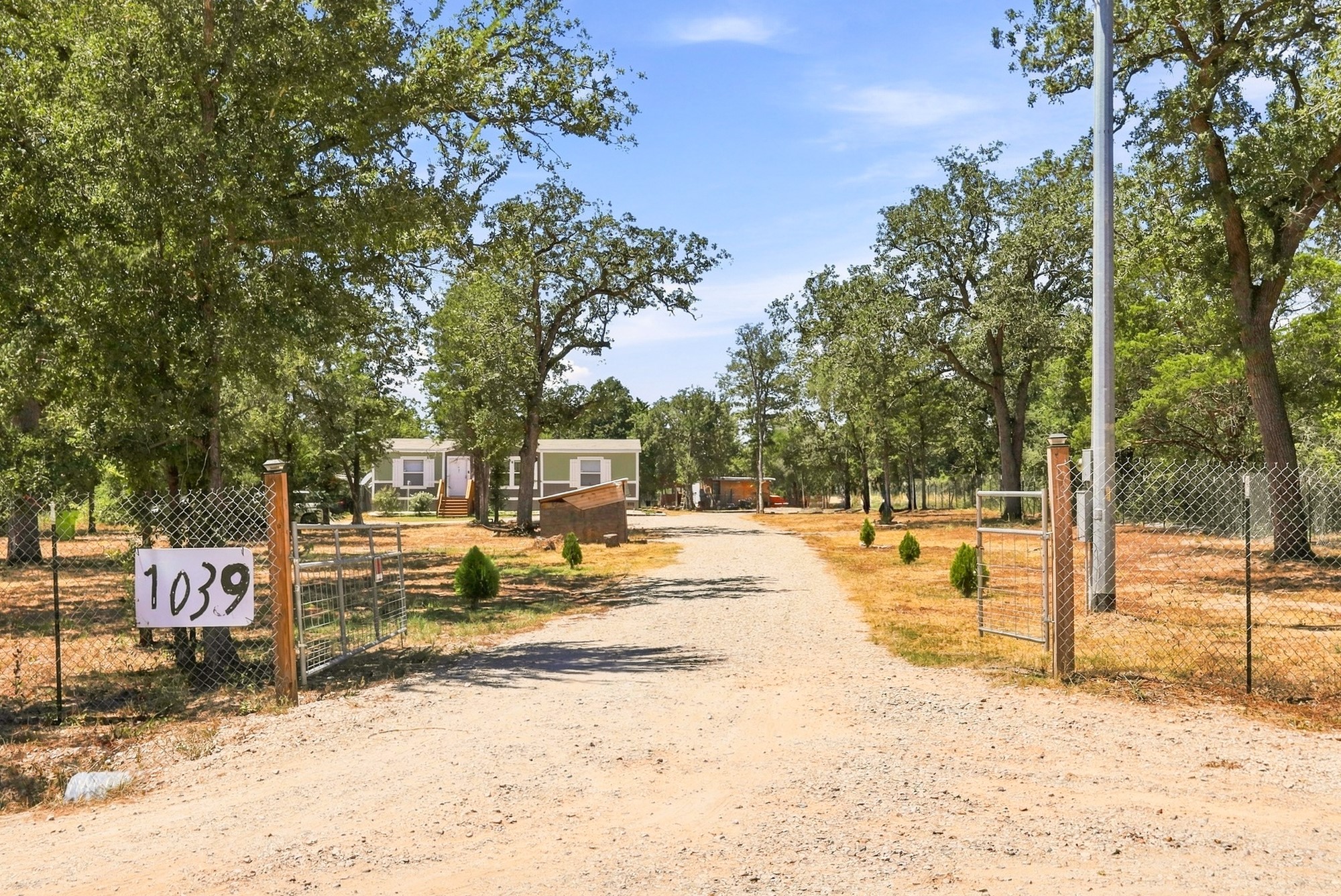 1039 Trailside Elgin, TX 78621 - Photo 1 of 24 Mature trees frame a private, gated entrance leading to a secluded rural residence.