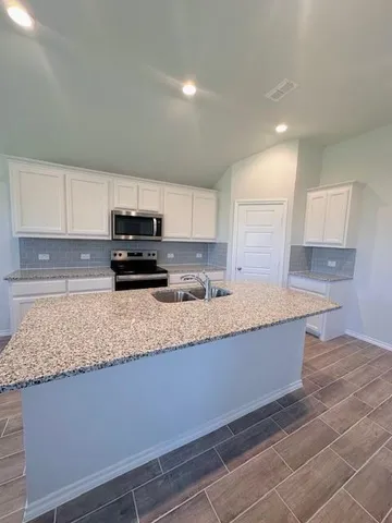 a kitchen with granite countertop a sink a stove top oven a counter top space and cabinets