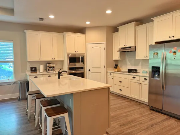 a kitchen with stainless steel appliances a stove a sink dishwasher a refrigerator with white cabinets and wooden floor