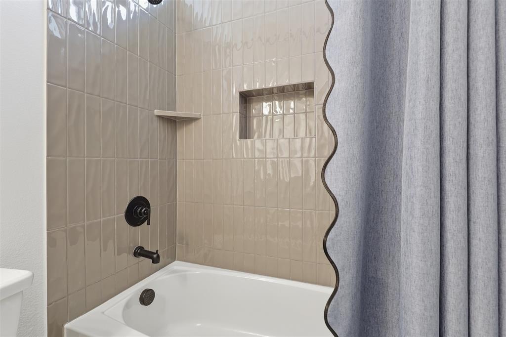 15413 Short Rdg Lane Fort Worth, TX 76008 - Photo 29 of 39 Bathtub with matte black fixtures, textured subway tile surround, recessed niche, and integrated shelf